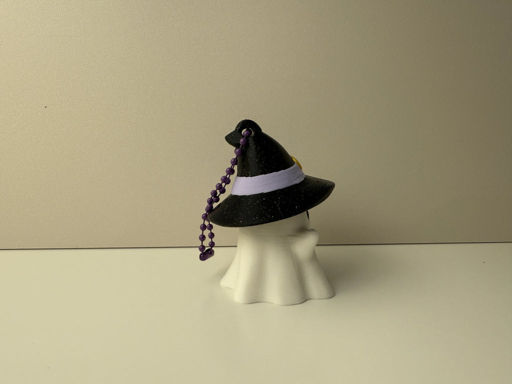 Black witch hat with a purple beaded ribbon on a white mannequin head against a beige background