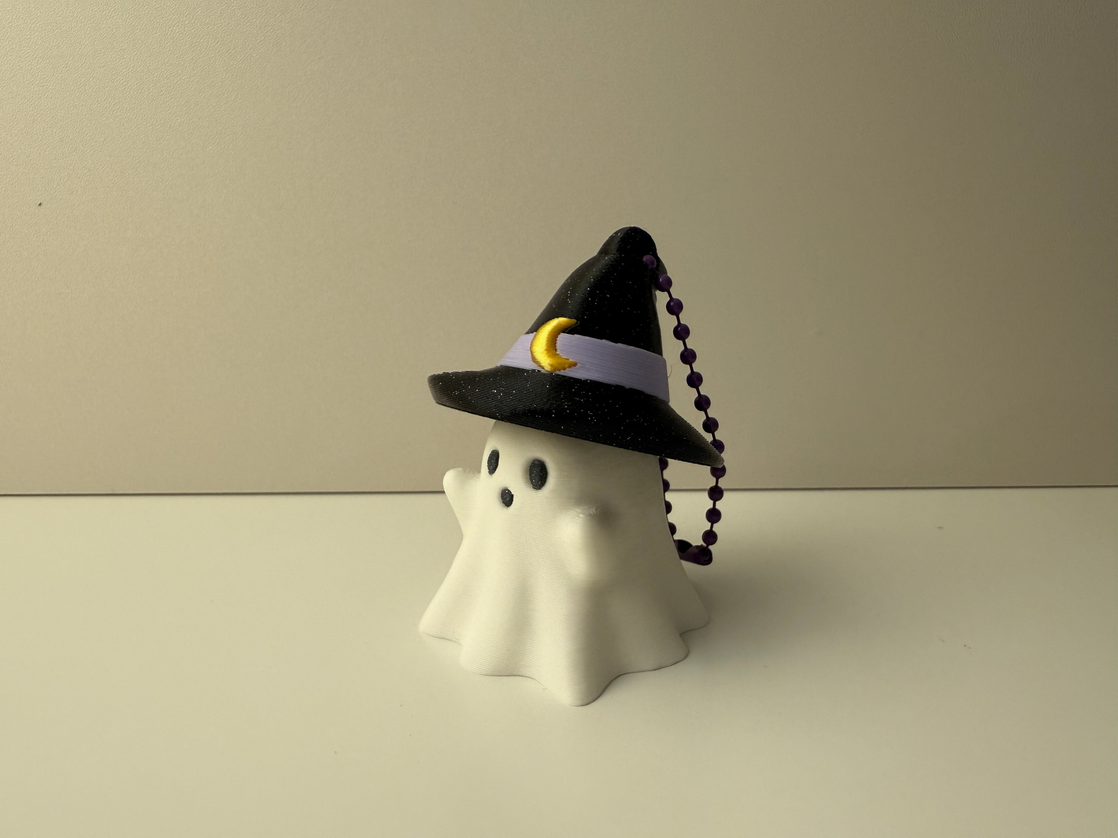 White ghost figurine with a black witch hat on a beige background