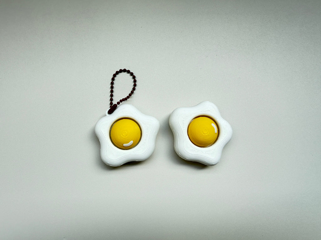 Fried egg-shaped keychains on a gray background