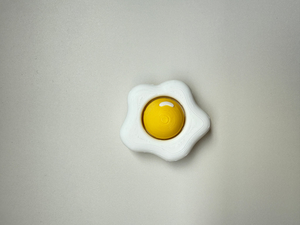 White toy resembling a fried egg with a yellow center on a gray background