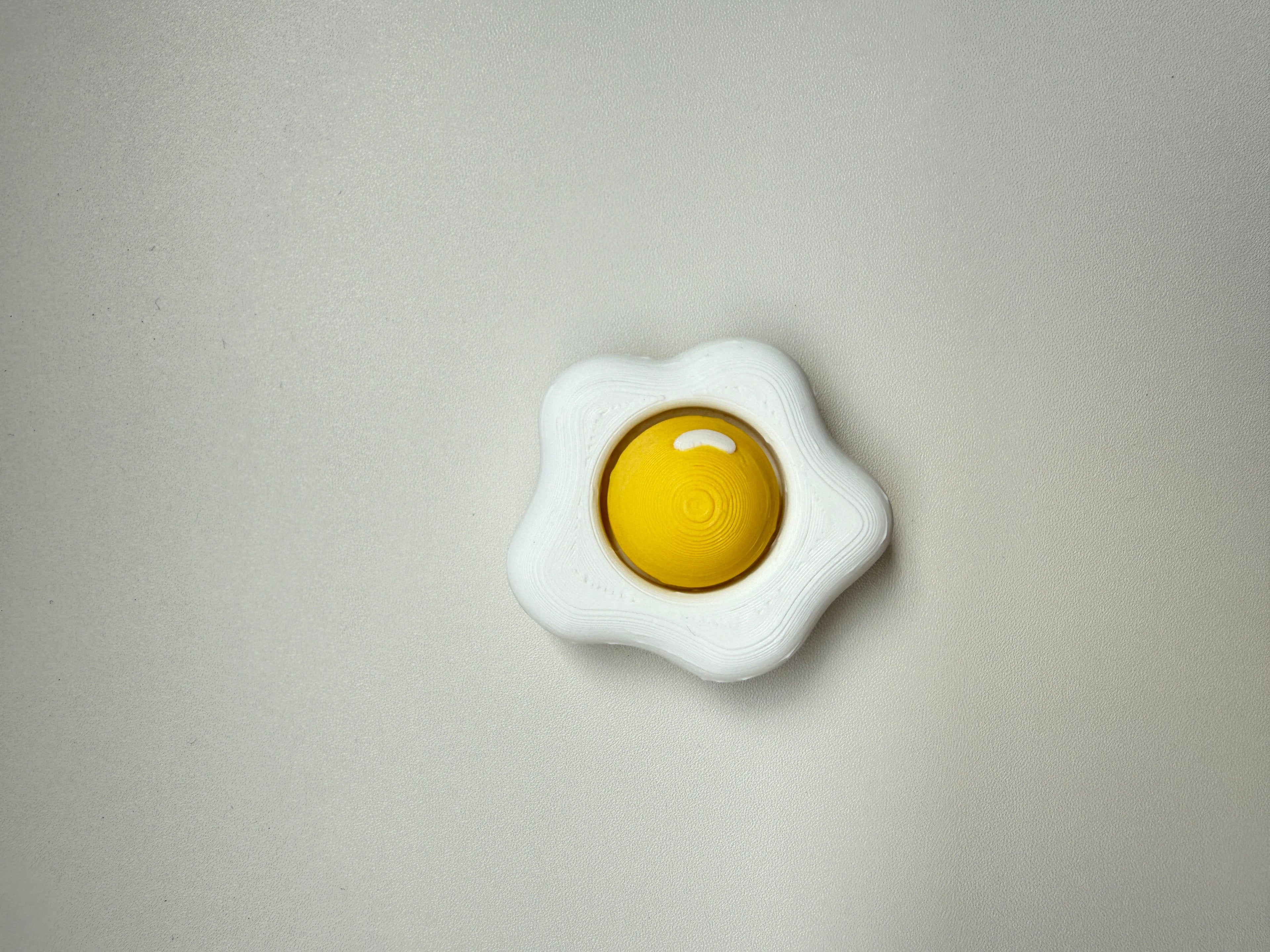 White toy resembling a fried egg with a yellow center on a gray background