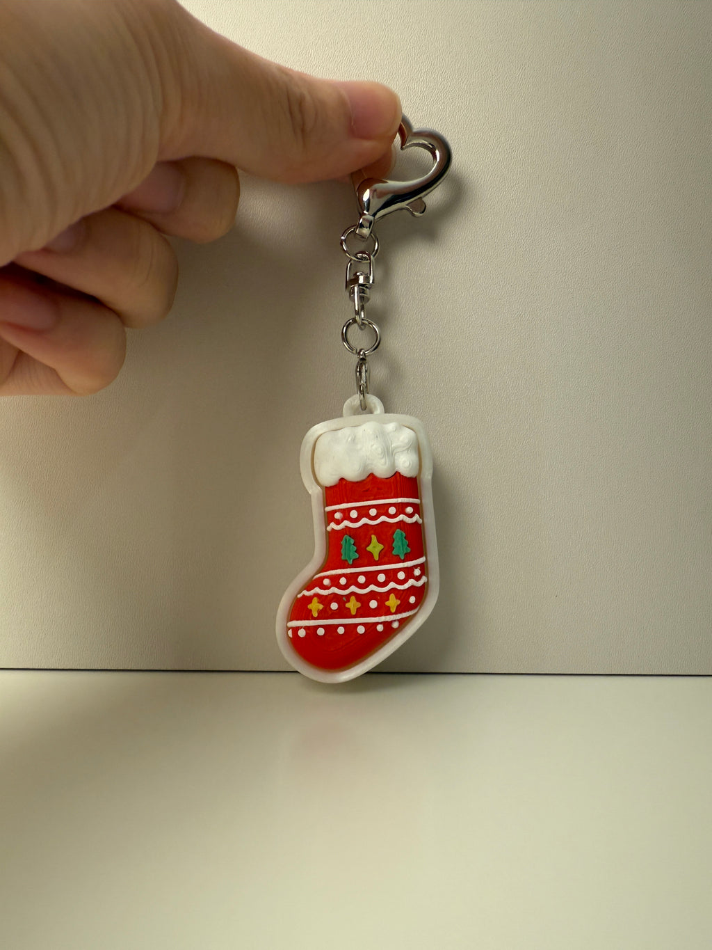 Keychain shaped like a red stocking with white snowflakes on a beige background