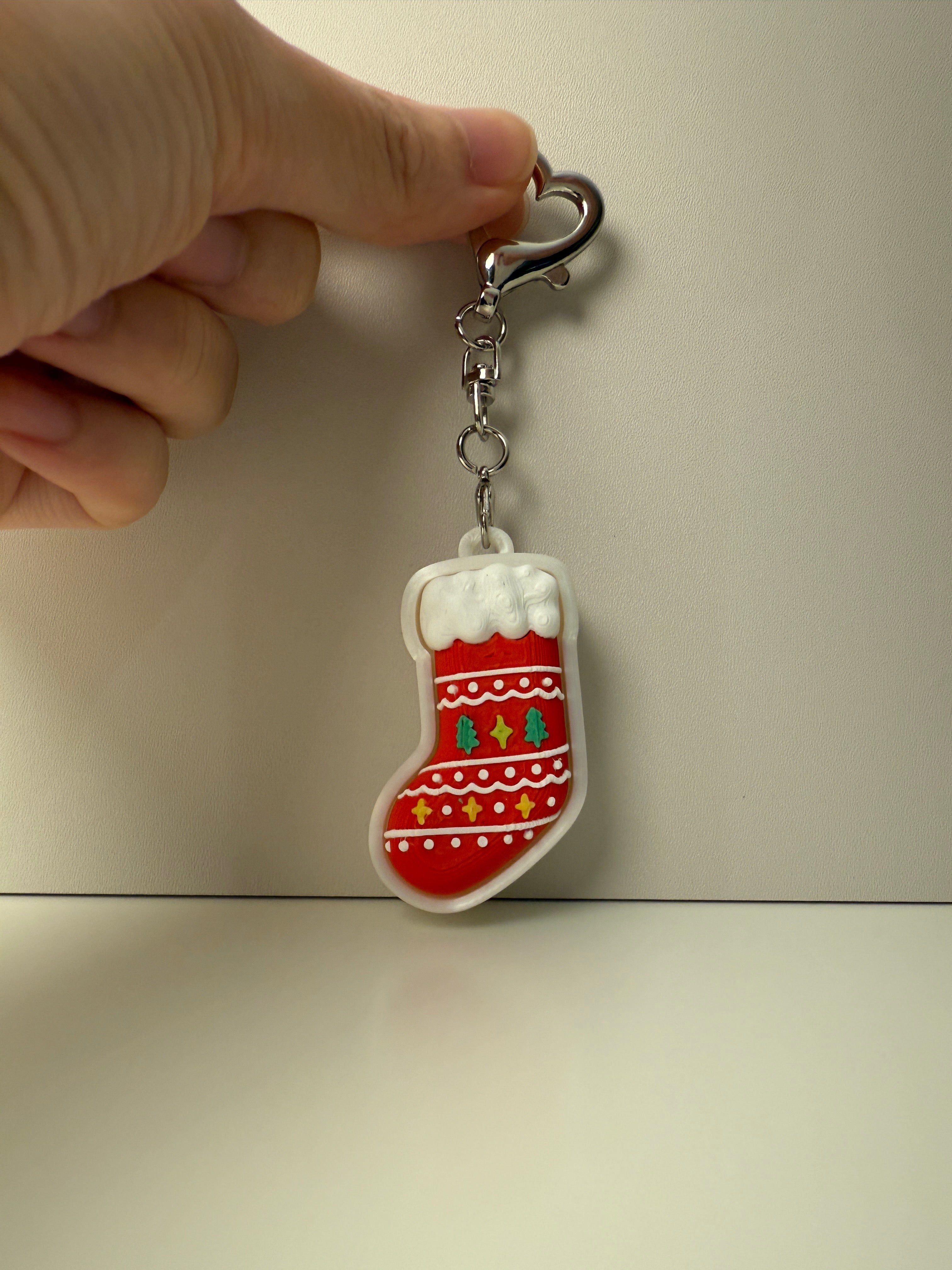 Keychain shaped like a red stocking with white snowflakes on a beige background