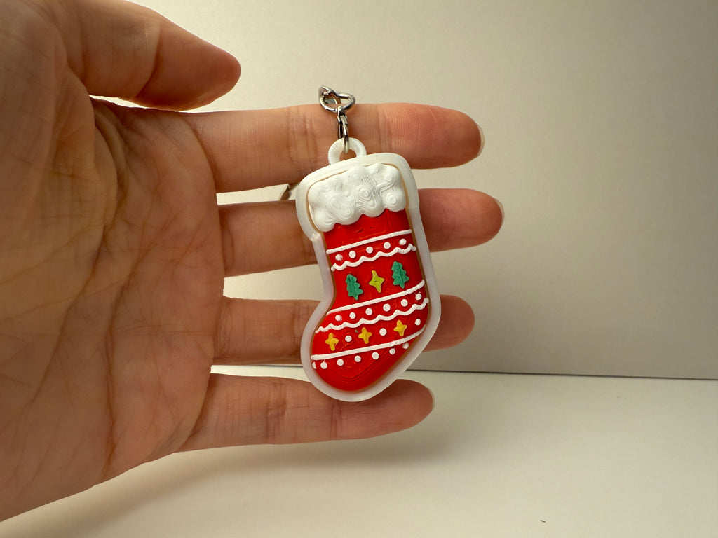 Hand holding a Christmas stocking keychain with decorative elements on a plain background