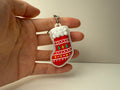 Hand holding a Christmas stocking keychain with decorative elements on a plain background