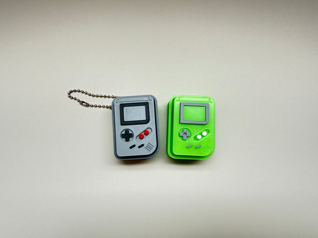 Two retro-style game console keychains, one gray and one green, on a plain background.
